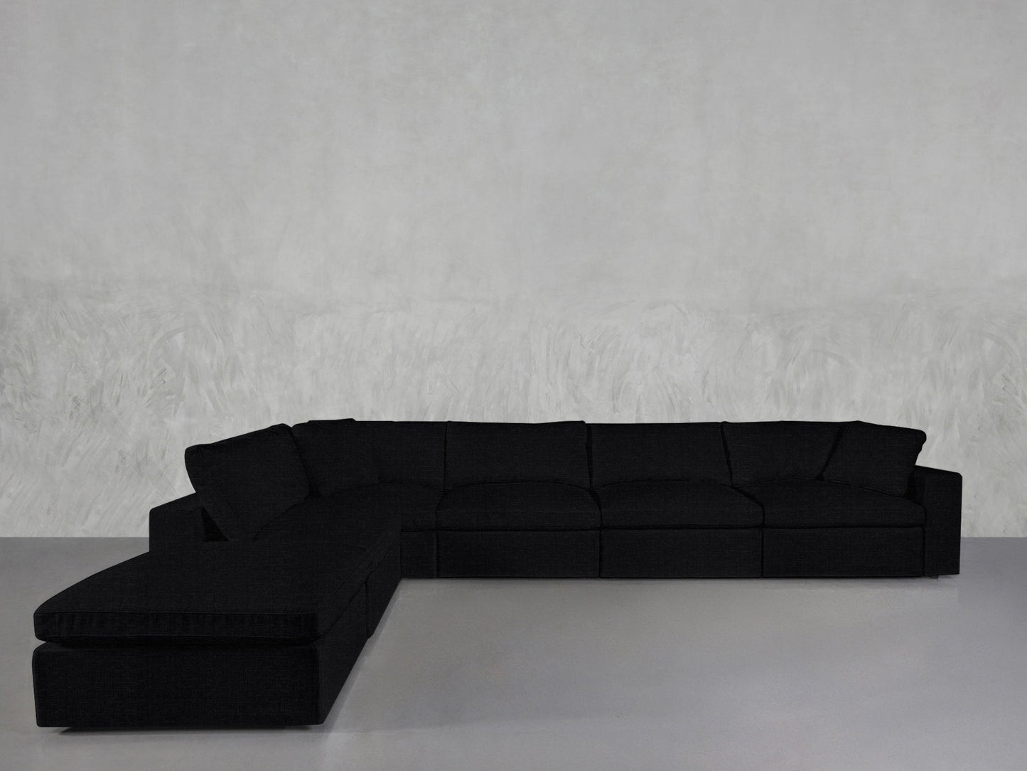 A spacious black 6-Seat Modular Corner Lounger Sectional with cushions sits in a minimalist room featuring a light gray textured wall and a smooth gray floor.