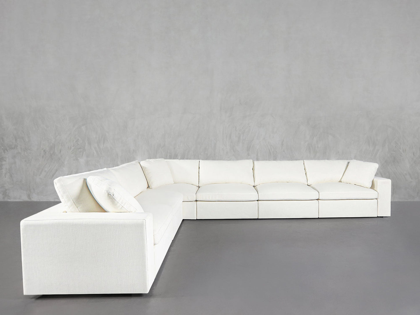 A 6-Seat Modular Corner Sectional in modern white with plush cushions sits against a plain light gray wall on a smooth gray floor.