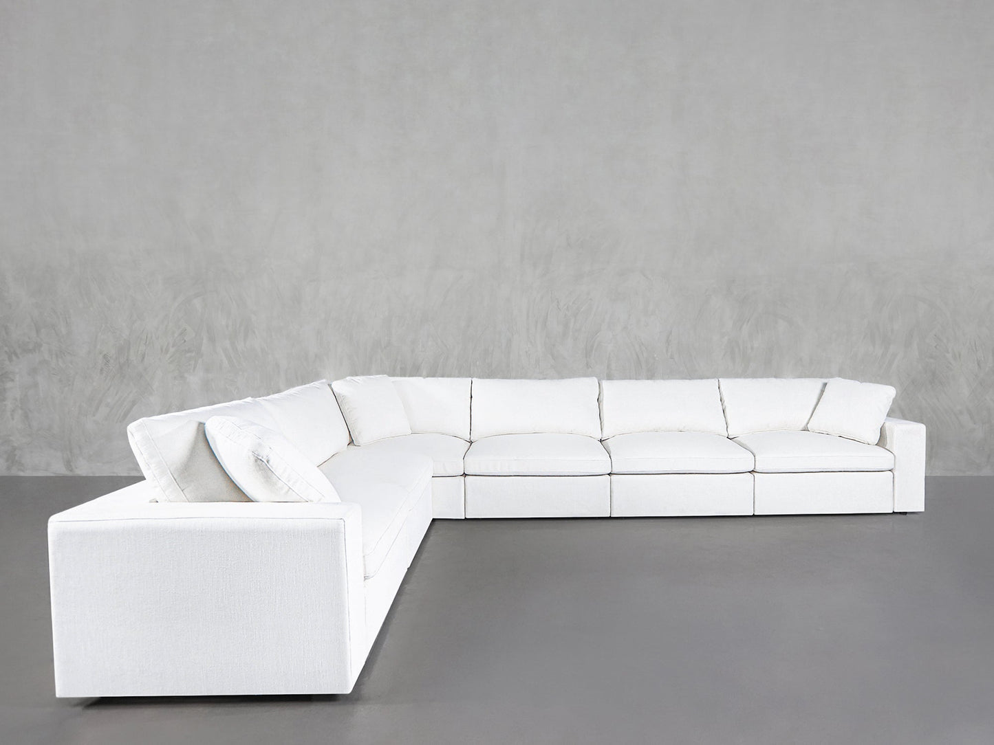 The 6-Seat Modular Corner Sectional, featuring a modern design with plush cushions and clean lines, is arranged in an L-shape against a plain gray textured wall and a gray floor.