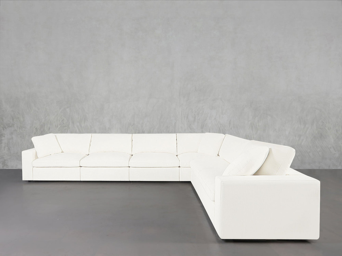 A 6-Seat Modular Corner Sectional with clean lines and plush cushions is set against a plain light gray wall and a smooth gray floor.