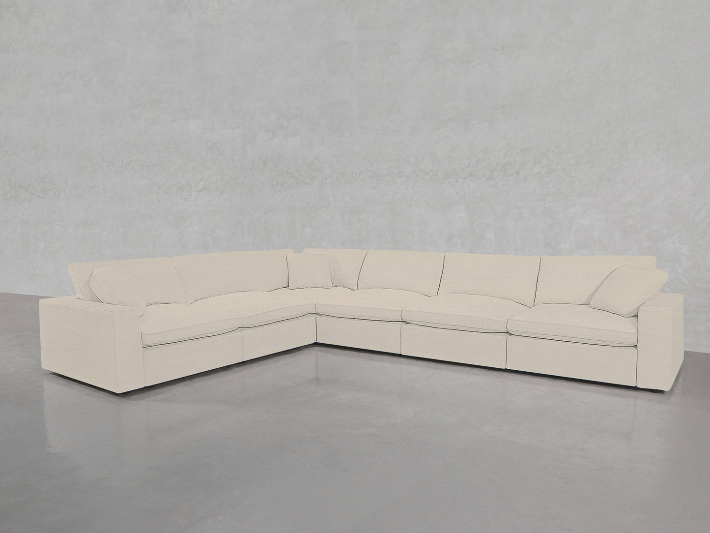 A spacious, modern 6-Seat Modular Corner Sectional with plush cushions is arranged in an L-shape against a plain light gray wall on a polished concrete floor.