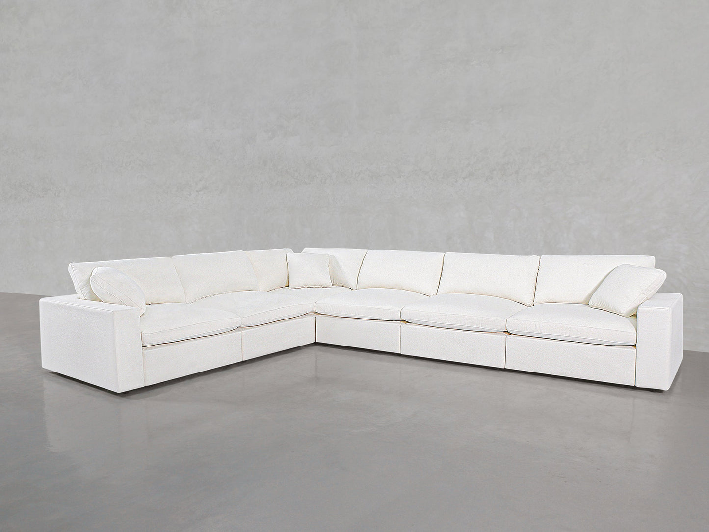 The 6-Seat Modular Corner Sectional, featuring plush cushions and clean lines, is arranged in an L-shape on a polished concrete floor against a light gray textured wall.