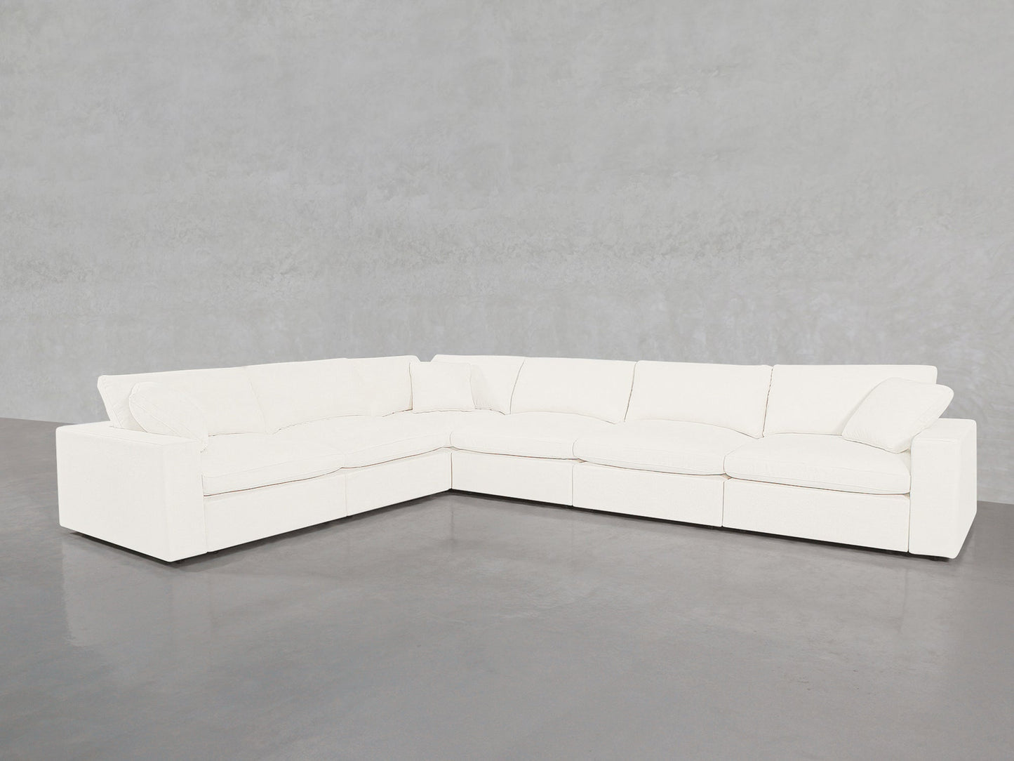 A 6-Seat Modular Corner Sectional with plush cushions sits on a smooth gray concrete floor against a light gray textured wall.
