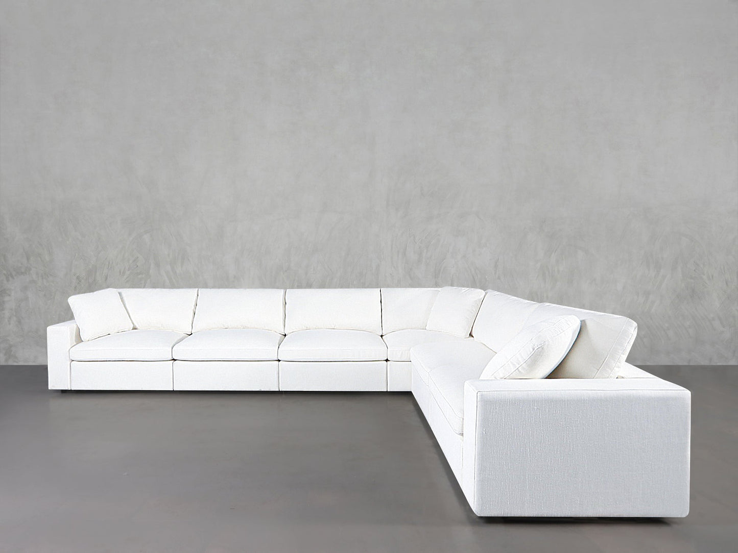 The 6-Seat Modular Corner Sectional features white upholstery, plush cushions, and a minimalist L-shaped design, arranged against plain gray walls and flooring.
