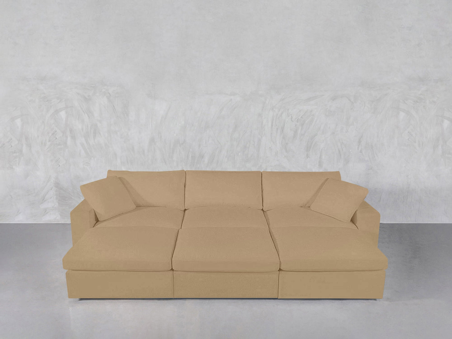 A beige 6-Seat Modular Daybed with matching cushions sits against a light gray textured wall on a smooth, reflective floor.