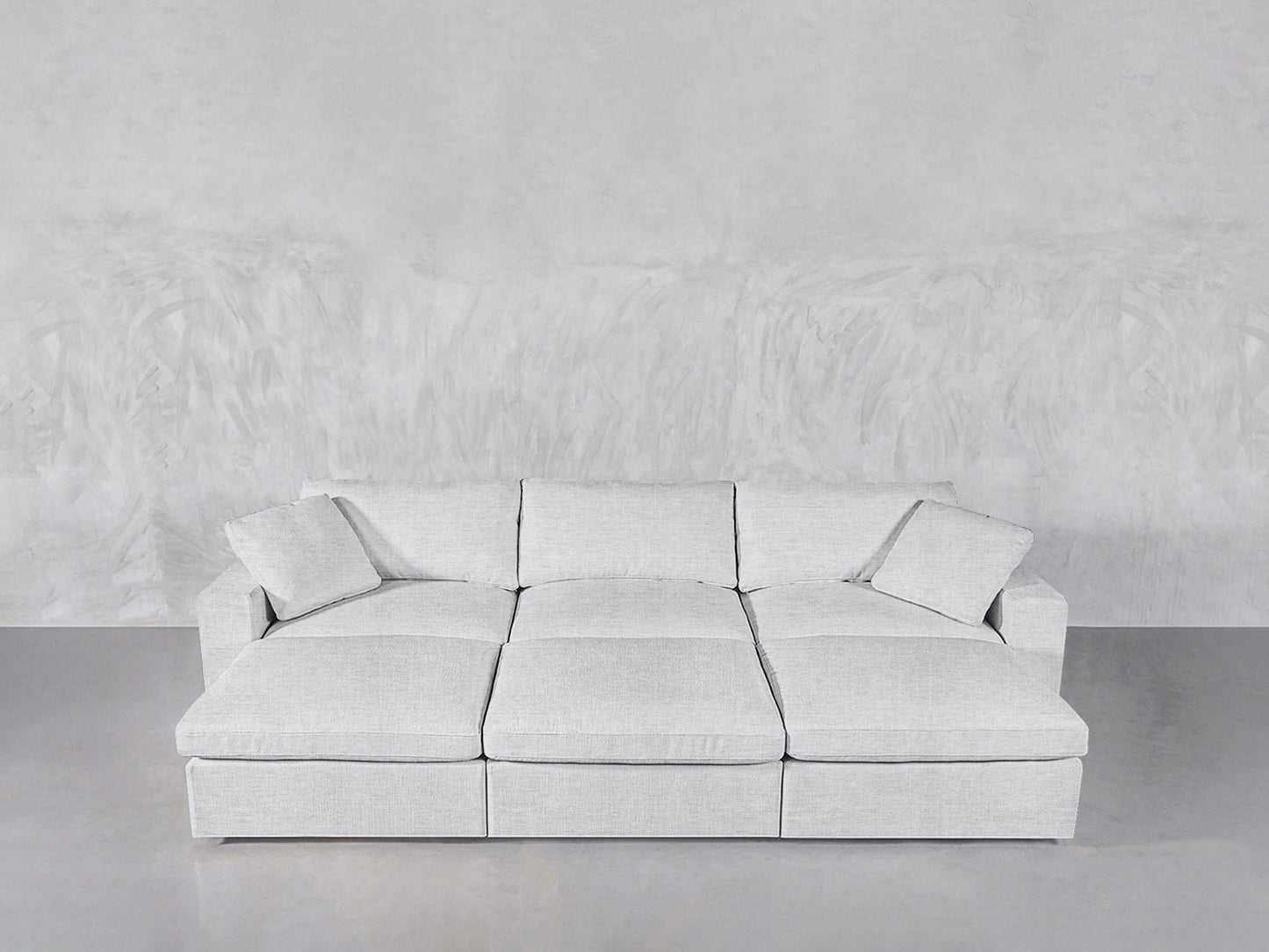 A modern, light gray 6-Seat Modular Daybed with matching cushions is set against a textured light gray wall atop a smooth concrete floor.
