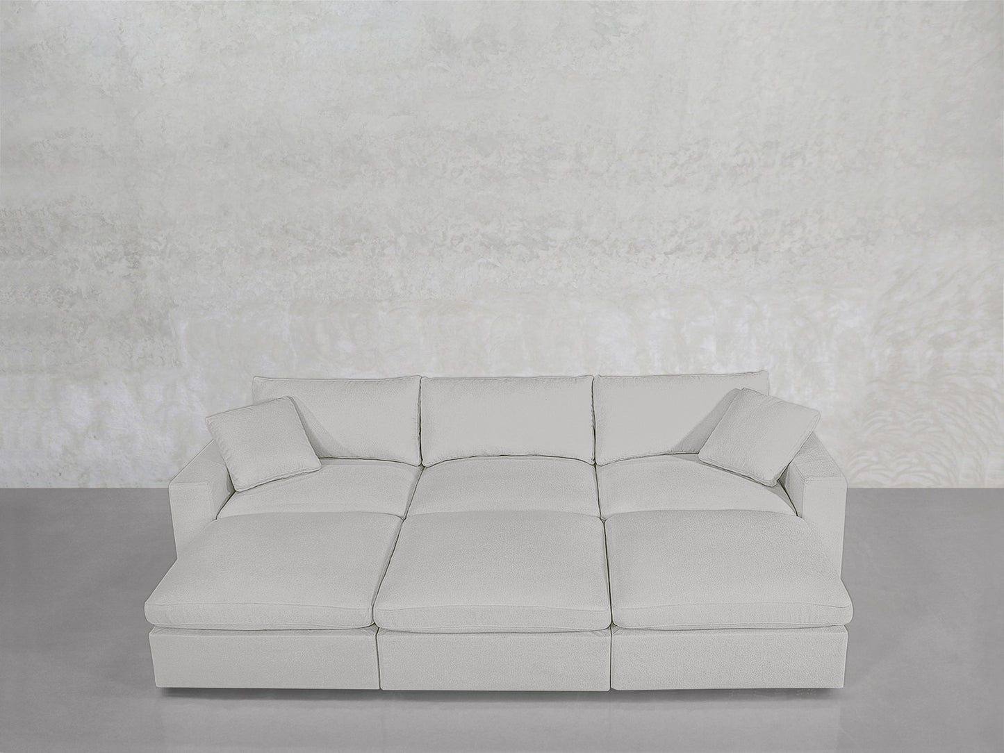 A modern, light gray 6-Seat Modular Daybed with matching cushions, set against a textured light gray wall and a smooth gray floor.