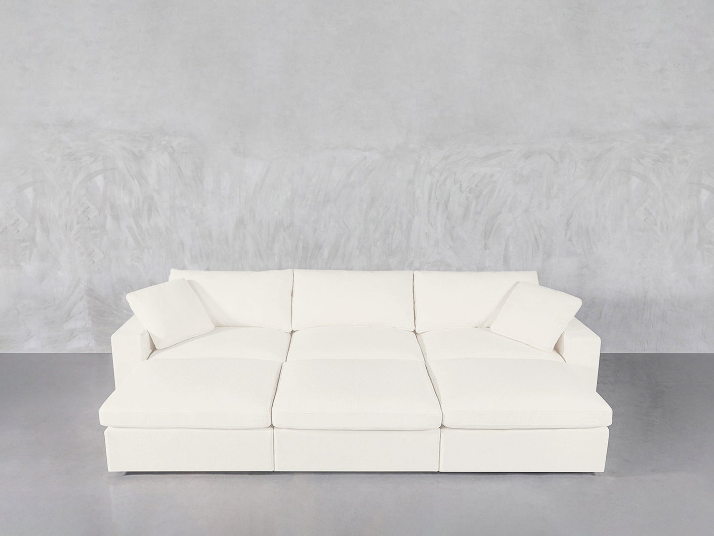 A modern 6-Seat Modular Daybed in white, featuring six seats and two matching square cushions, set against a light gray textured wall and smooth gray floor.