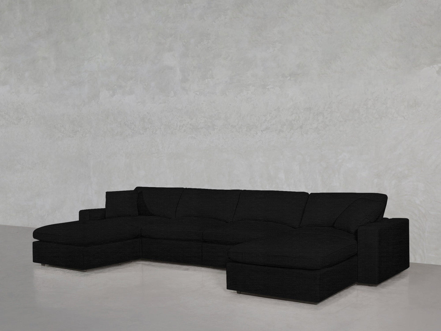 The 6-Seat Modular Double Chaise Sectional, featuring wide black seats and cushions in an L-shape, is placed against a light gray textured wall on a shiny light-colored floor.