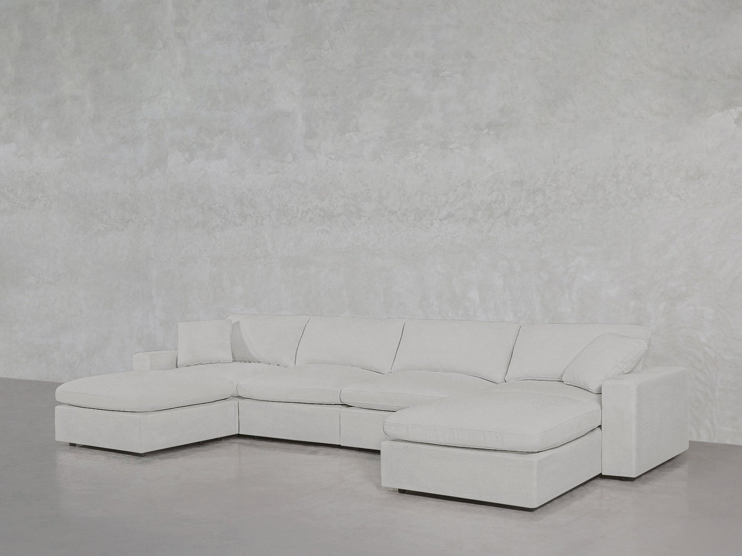 The 6-Seat Modular Double Chaise Sectional in light gray sits against a matching textured wall and smooth floor, creating a modern, minimalist atmosphere.