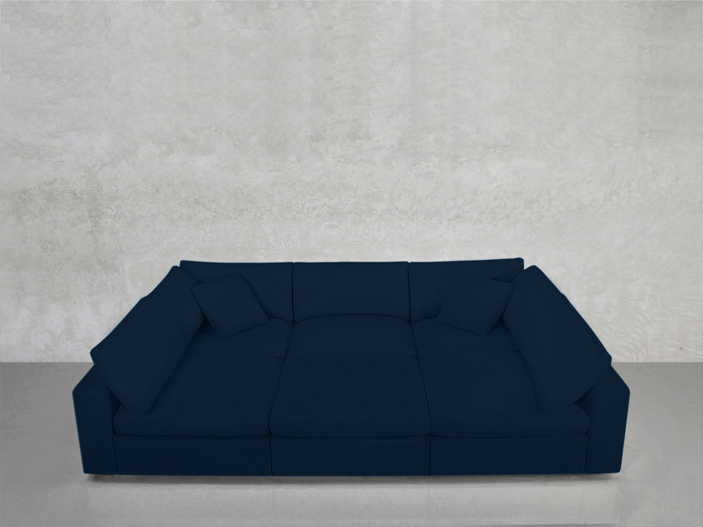 A 6-Seat Modular Pit in dark blue with square cushions sits against a light gray textured wall on a glossy floor.