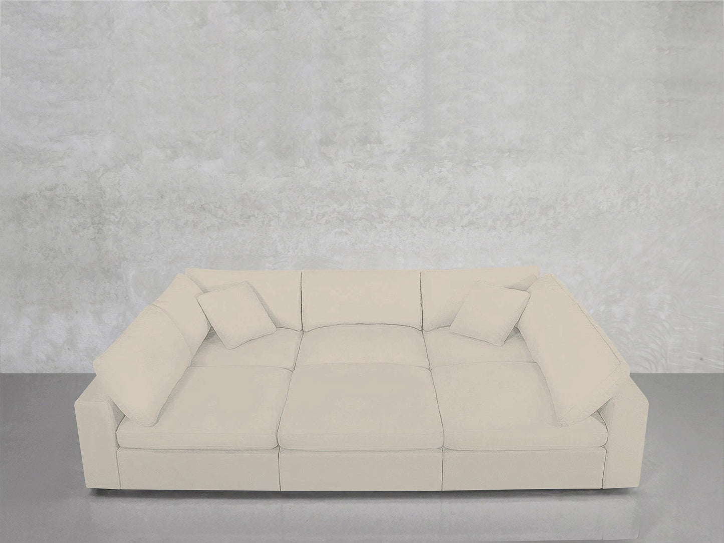 A contemporary 6-Seat Modular Pit in white, complete with four matching square cushions, is positioned against a light gray textured wall atop a glossy gray floor.