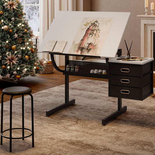 The Adjustable Drafting Drawing Table With Stool And 3 Drawers - White / Black is shown with watercolor art, an open notebook, and paint jars. A matching stool stands nearby, with a Christmas tree and lit fireplace candles in the background.