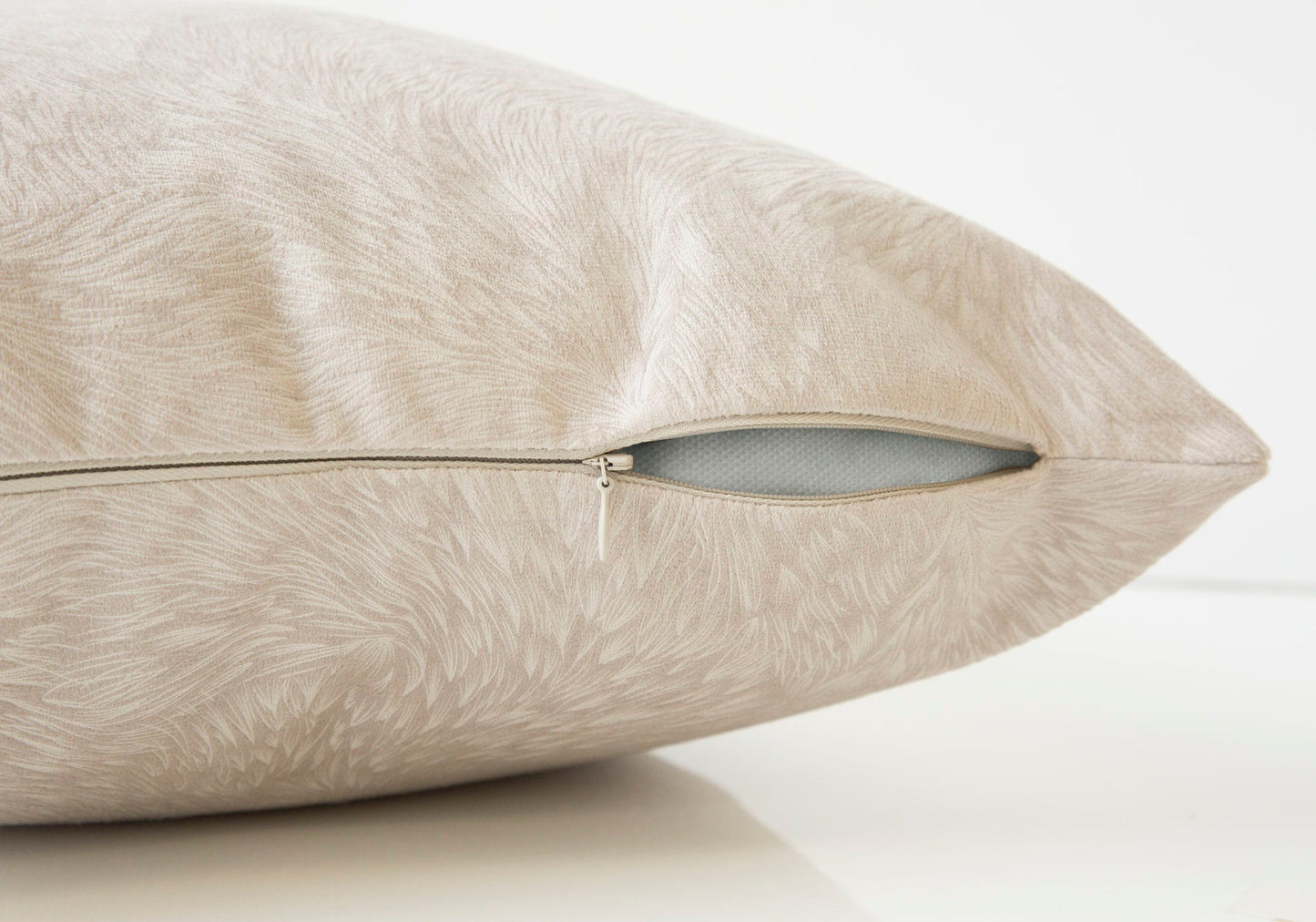 Close-up of a beige Modern Square Decorative Throw Pillow with a subtle leaf pattern and partially open zipper revealing the white hypoallergenic insert. Plain, light-colored background. Insert included.