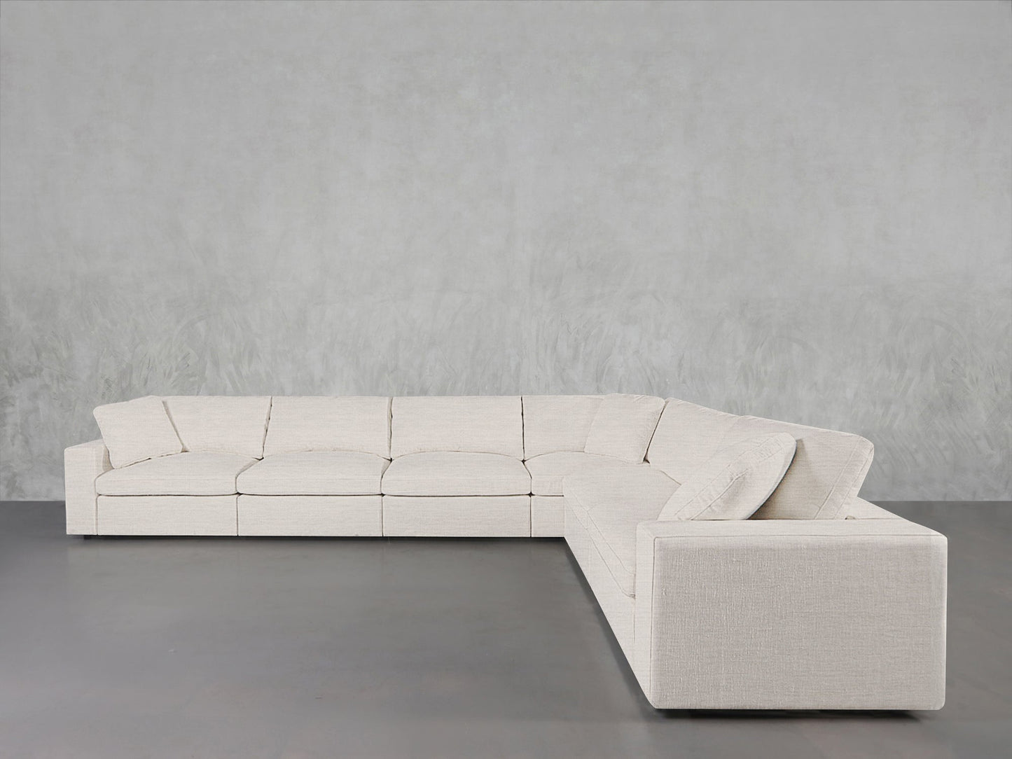 A 6-Seat Modular Corner Sectional with light beige fabric upholstery sits in a minimalist room featuring a gray concrete floor and pale gray textured wall.
