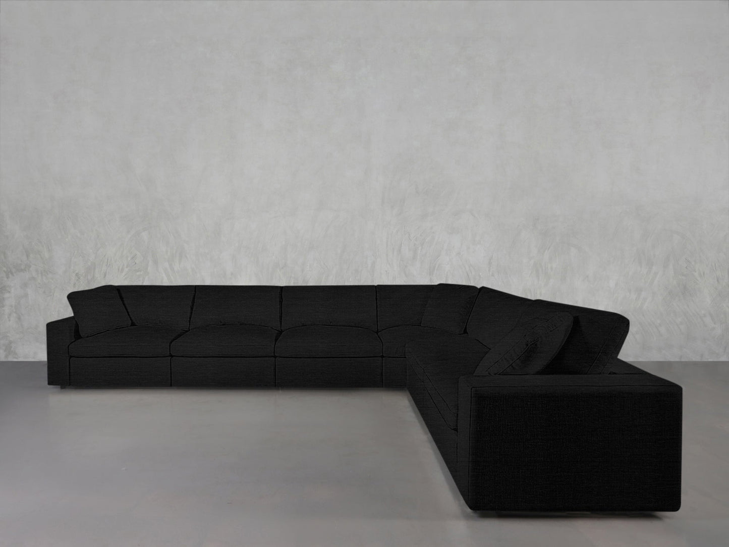 A 6-Seat Modular Corner Sectional with clean lines in black is arranged on a light gray concrete floor against a plain, textured light gray wall.