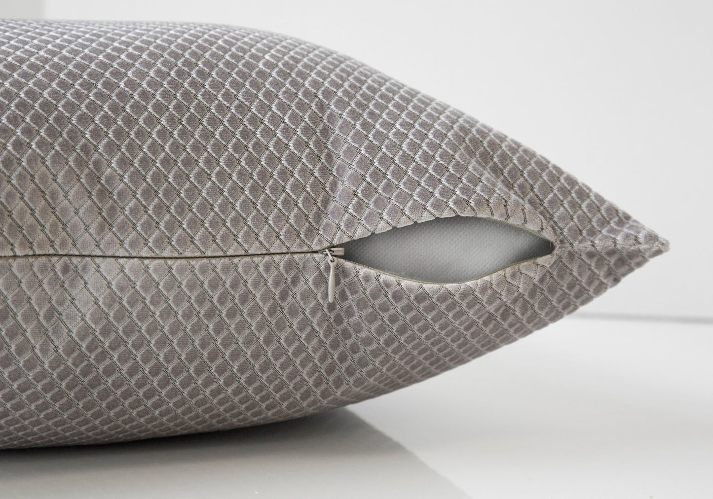 A close-up of a decorative gray modern square pillow with a diamond pattern, featuring a partially open zipper showing the hypoallergenic insert. The background is plain white.