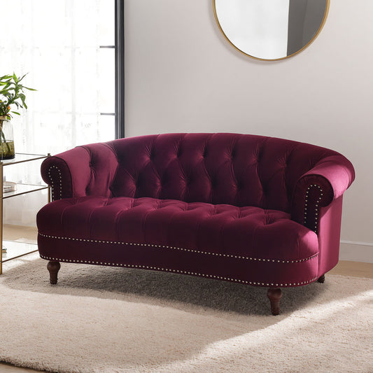 The La Rosa - Victorian Chesterfield Loveseat, upholstered in deep purple velvet with tufted details, nailhead trim, and rolled arms, sits on a light beige rug in a bright room near a glass table, plant, and round wall mirror.