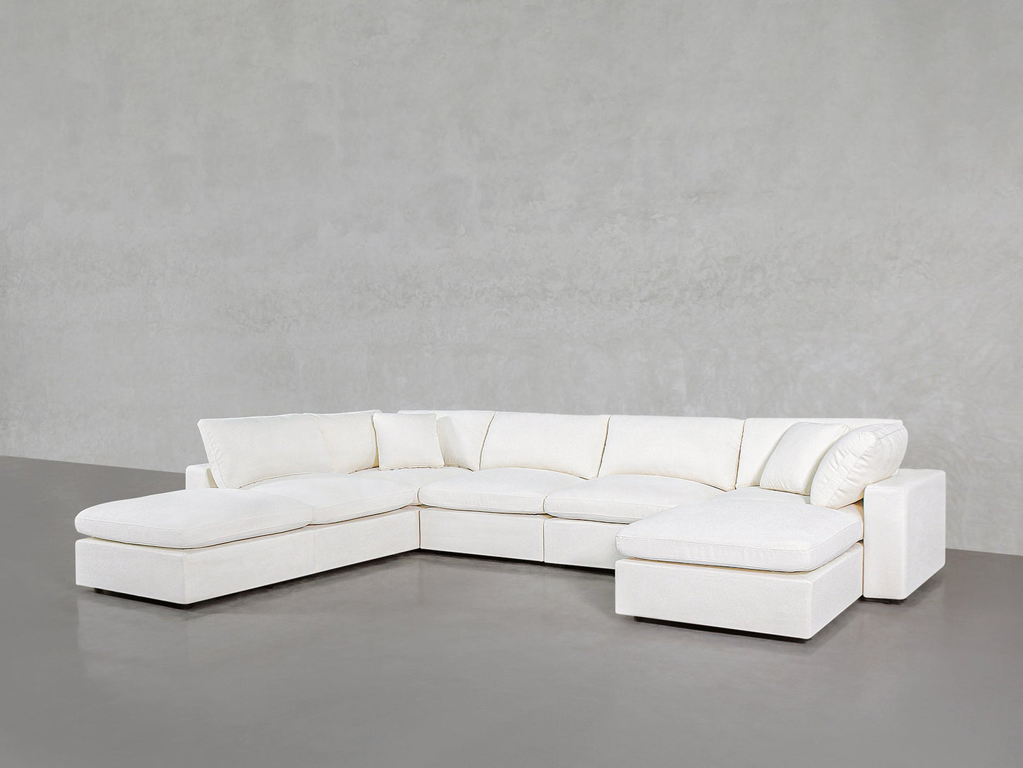 The 7-Seat Modular Chaise Corner Lounger Sectional, featuring a modern white design with clean lines and plush cushions, sits on a smooth gray concrete floor against a light gray textured wall.