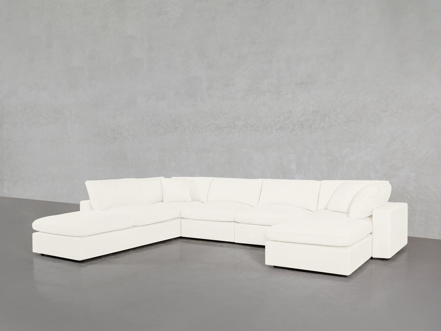 A 7-Seat Modular Chaise Corner Lounger Sectional with plush cushions, in a modern white design, sits against a light gray wall and dark gray floor in a minimalistic room.