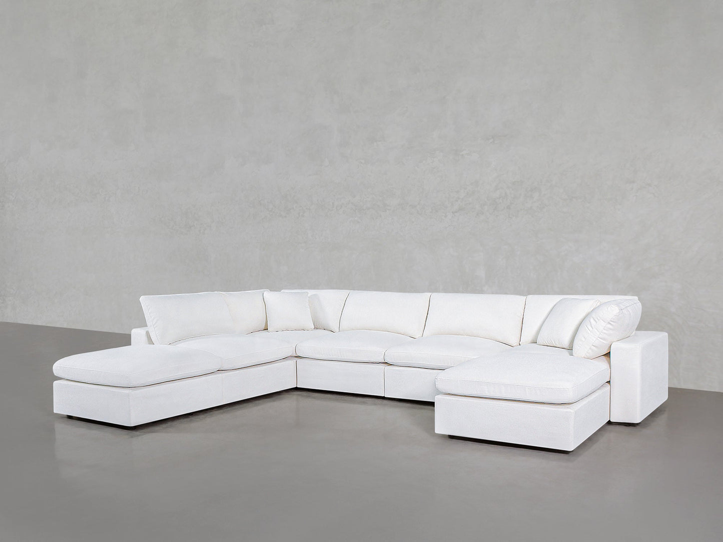 The 7-Seat Modular Chaise Corner Lounger Sectional, featuring plush white cushions, is arranged in an L-shape along a plain light gray wall and floor.