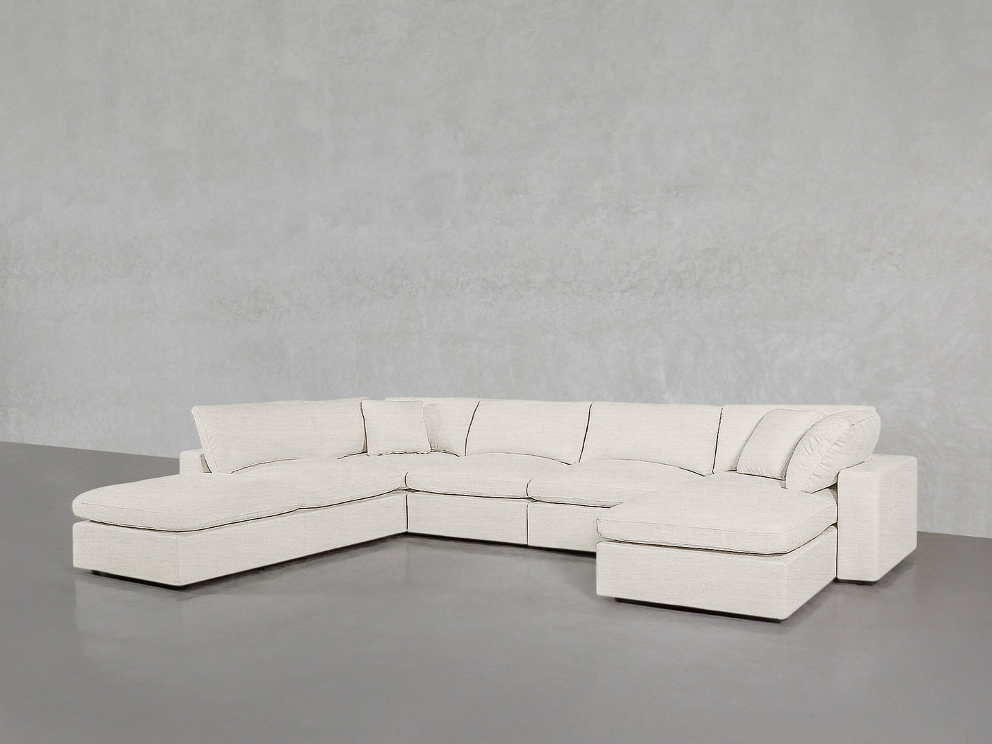 The 7-Seat Modular Chaise Corner Lounger Sectional, upholstered in light beige, sits in a minimalistic room with a plain gray wall and floor, featuring chaise lounges on both the left and right sides.