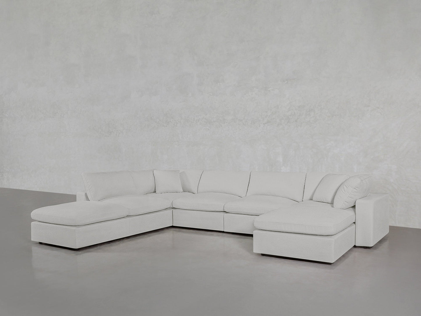 The 7-Seat Modular Chaise Corner Lounger Sectional in light gray features chaise lounges on both ends and sits on a polished concrete floor against a textured light gray wall.