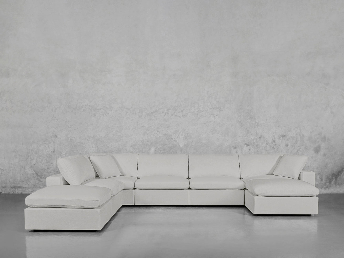 A spacious 7-Seat Modular Chaise Corner Lounger Sectional in light gray with clean lines and wide cushions sits against matching textured gray walls and flooring, enhancing the minimalist room.