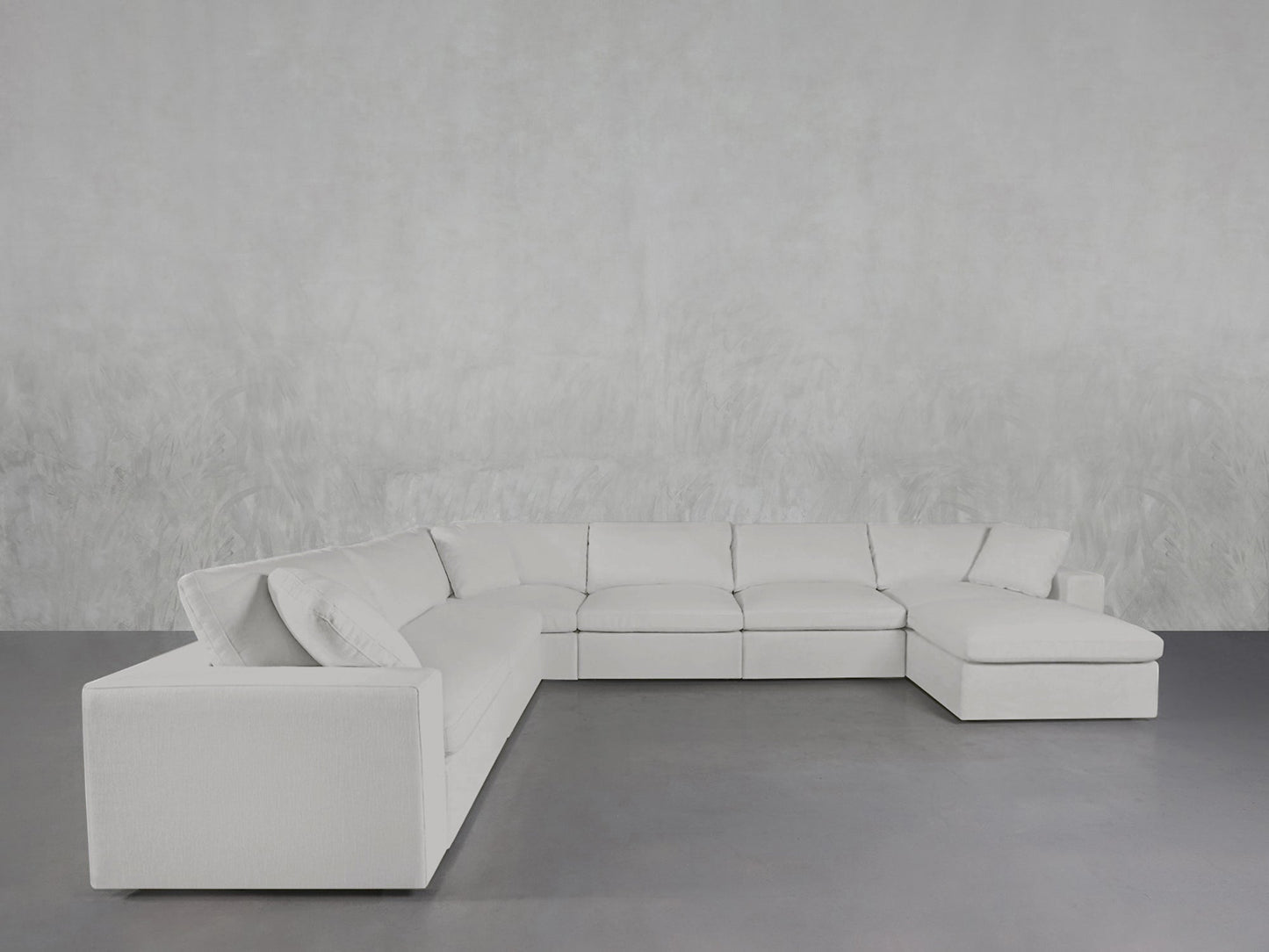 A 7-Seat Modular Chaise Corner Sectional in modern white is placed against a light gray textured wall on a smooth gray floor in a minimalist room.
