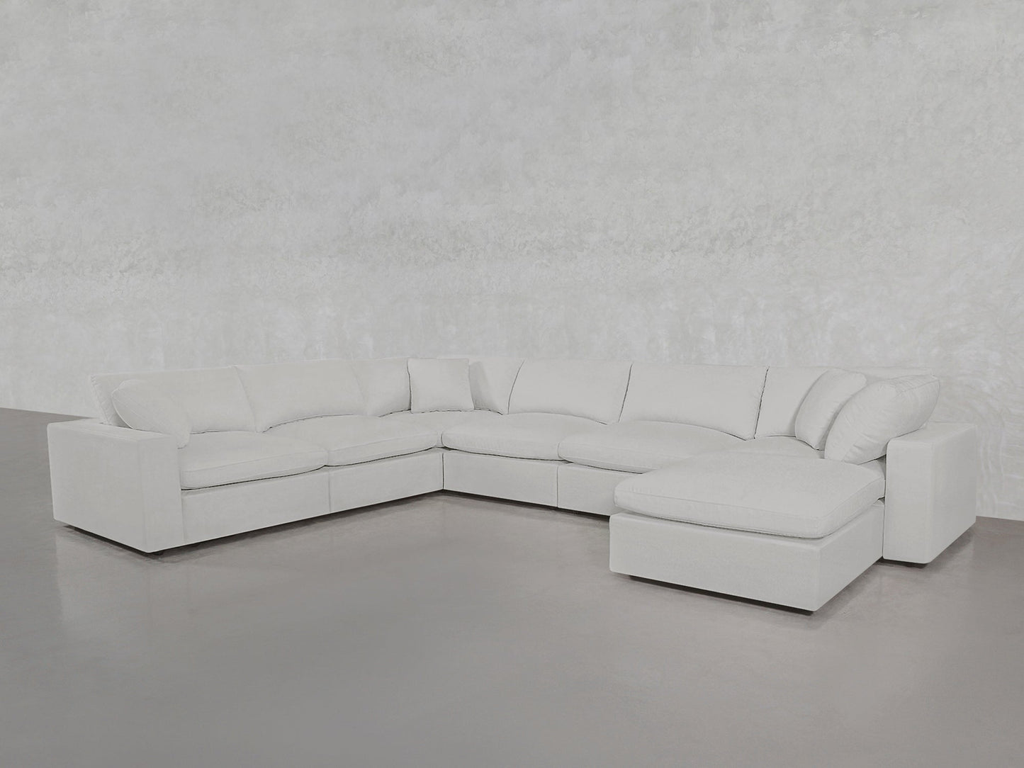 The 7-Seat Modular Chaise Corner Sectional, featuring multiple seat and back cushions, is showcased in a minimalist room with light gray walls and a smooth gray floor.