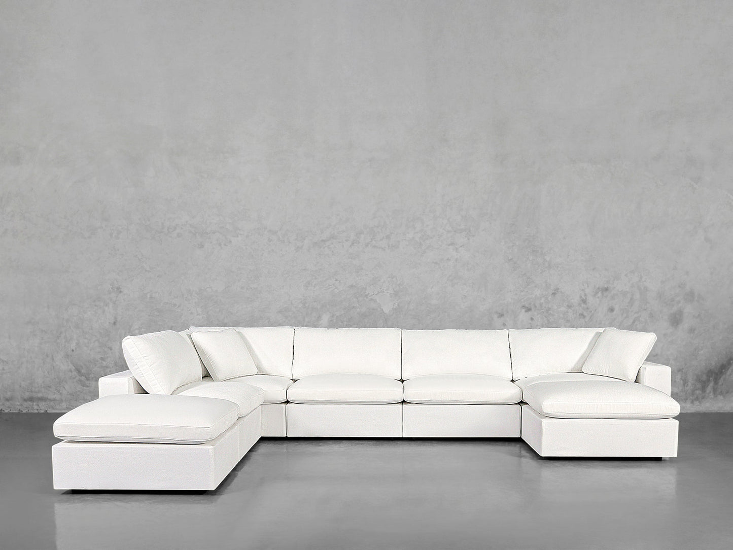 The 7-Seat Modular Chaise Corner Lounger Sectional, with its modern design and plush cushions, sits against a light gray textured wall on a smooth gray floor.