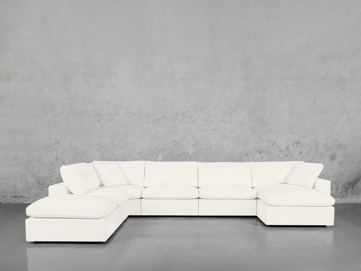The 7-Seat Modular Chaise Corner Lounger Sectional with plush white cushions sits in an empty room, highlighted by a smooth gray floor and a textured gray wall background.