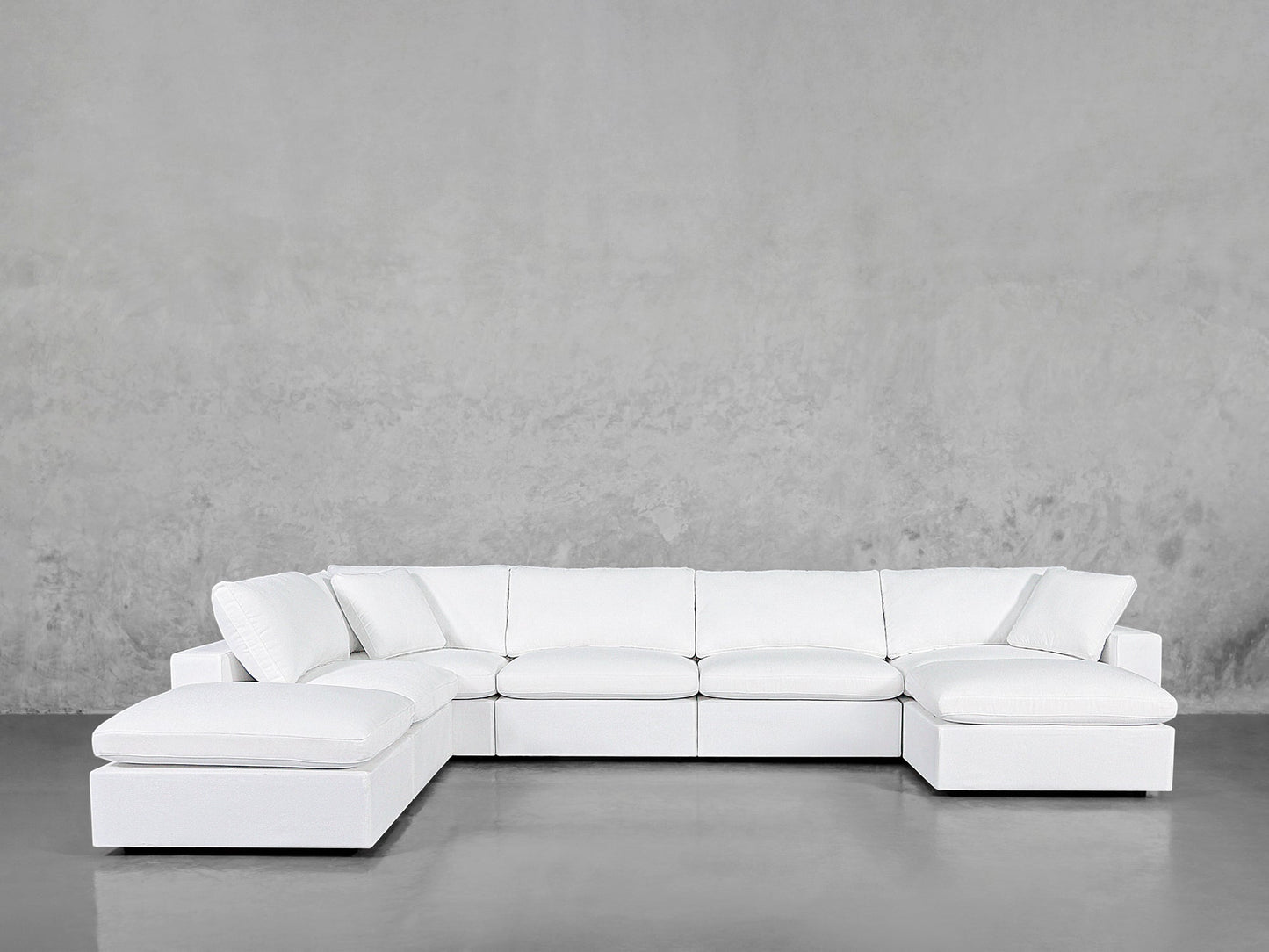 The 7-Seat Modular Chaise Corner Lounger Sectional with plush cushions sits against a textured gray wall on a smooth, reflective floor.