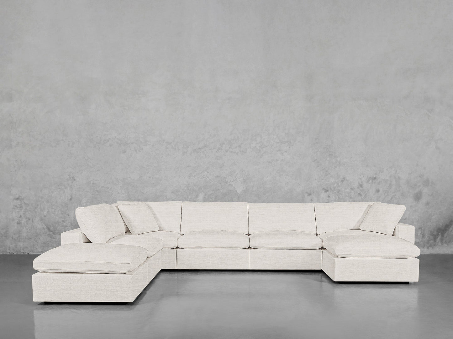 The 7-Seat Modular Chaise Corner Lounger Sectional in light beige fabric sits against a plain concrete wall and a polished gray floor.
