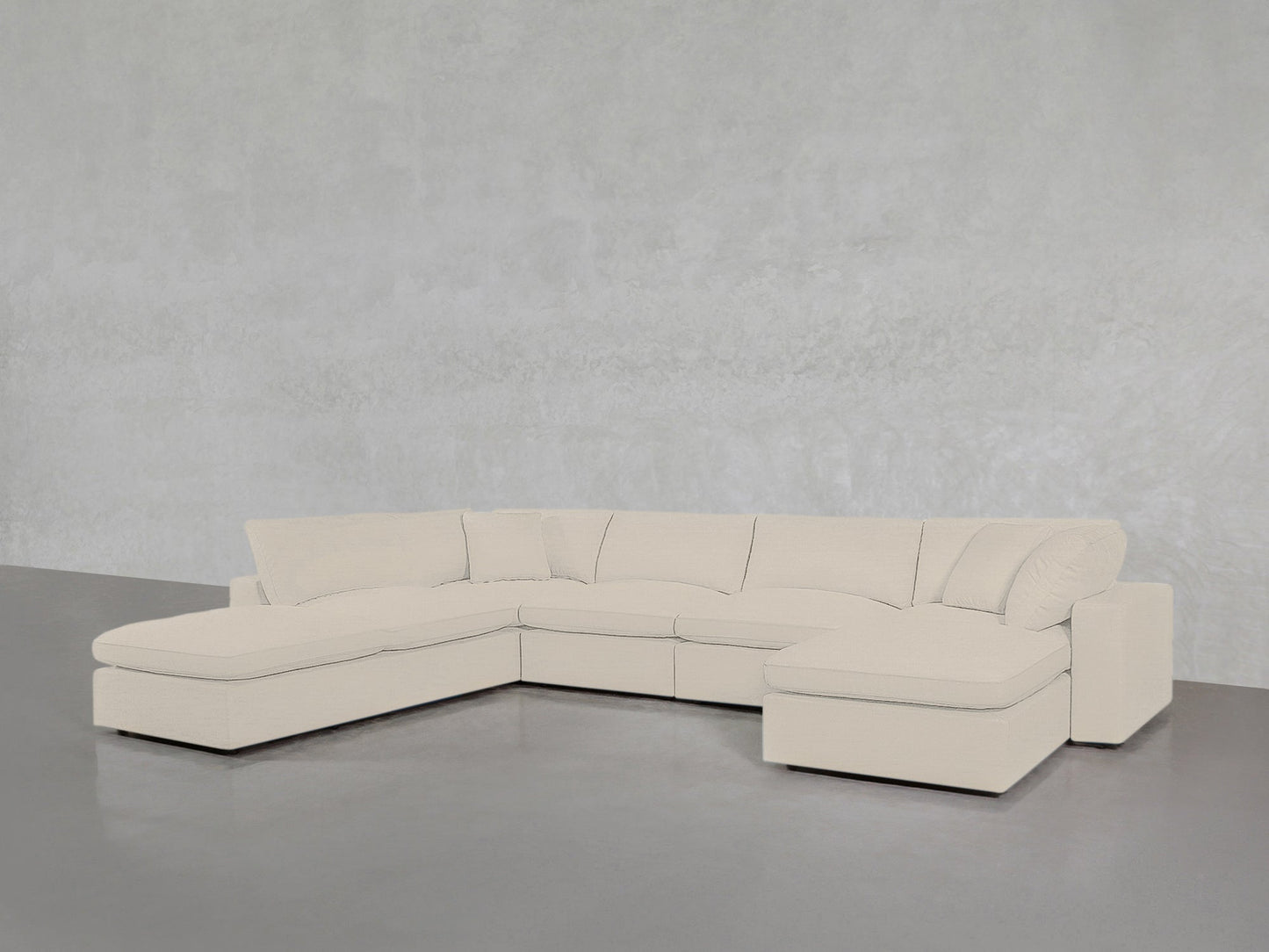 A 7-Seat Modular Chaise Corner Lounger Sectional in light beige with plush cushions and chaise lounges on both ends is placed against a plain, light gray textured wall on a smooth gray floor.