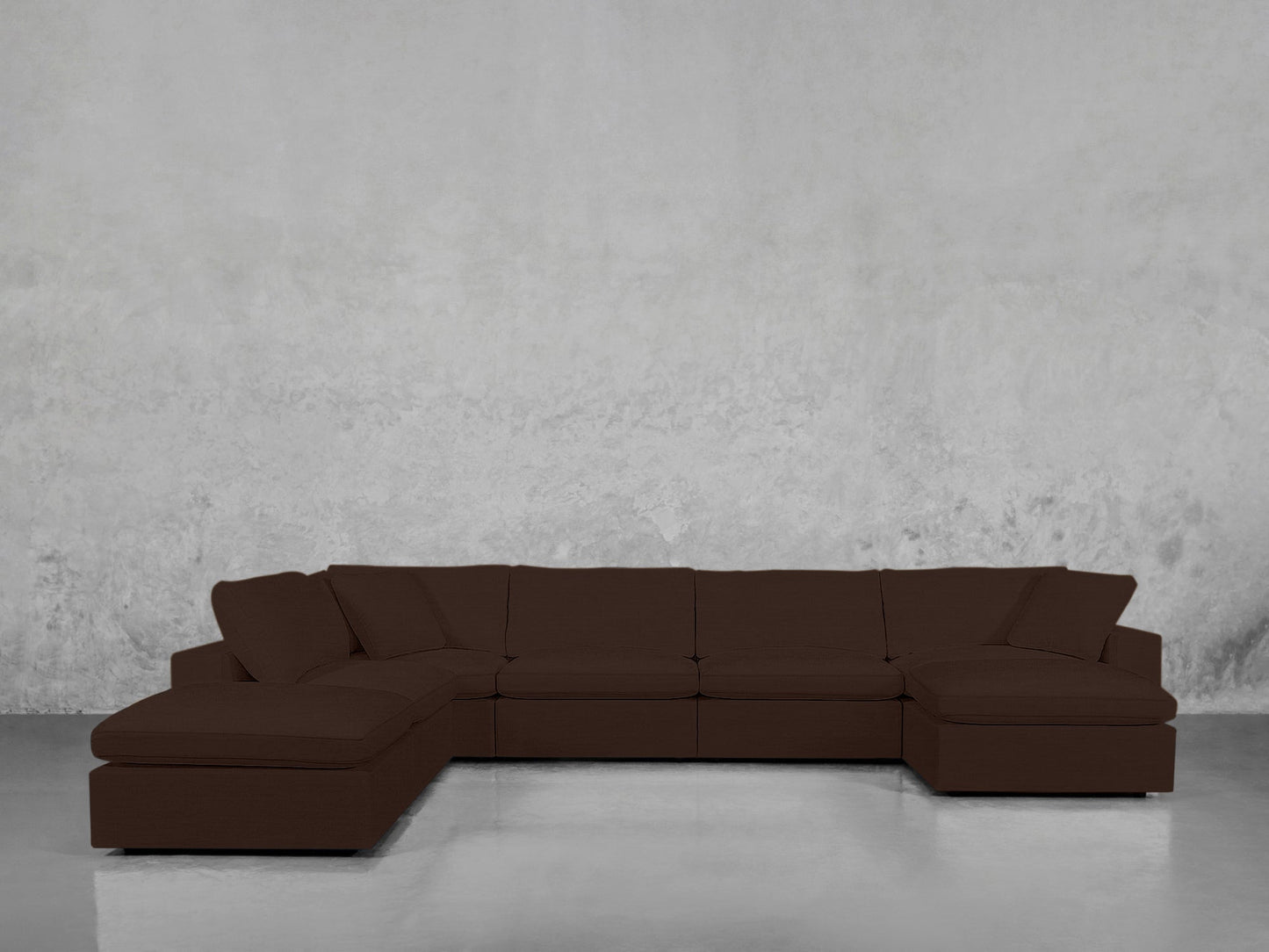A 7-Seat Modular Chaise Corner Lounger Sectional in dark brown with wide seats and cushions is placed against a plain, light gray textured wall on a shiny, light-colored floor.