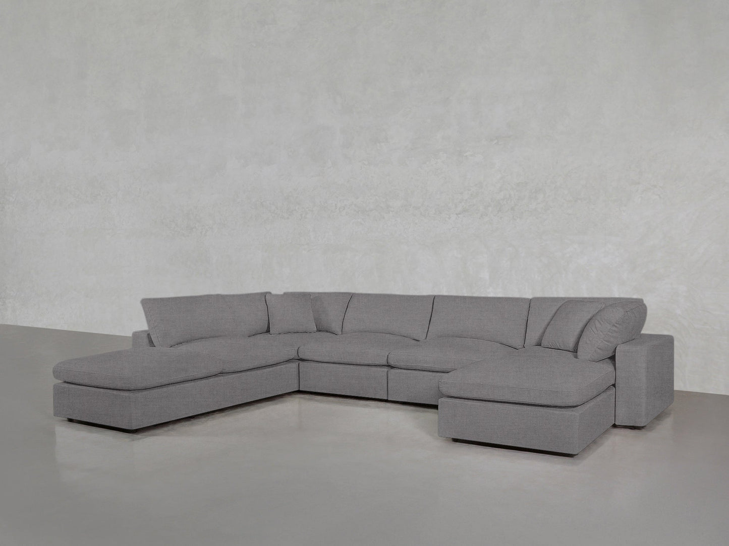 A 7-Seat Modular Chaise Corner Lounger Sectional with plush cushions and clean lines sits on a smooth cement floor against a light gray textured wall.