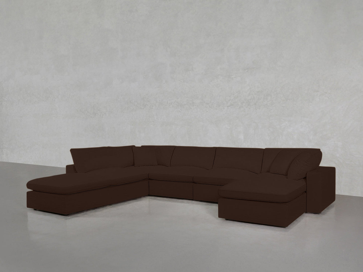 A 7-Seat Modular Chaise Corner Lounger Sectional in dark brown with cushions and a chaise lounge on one end sits on a smooth, light gray floor against a plain light gray wall.