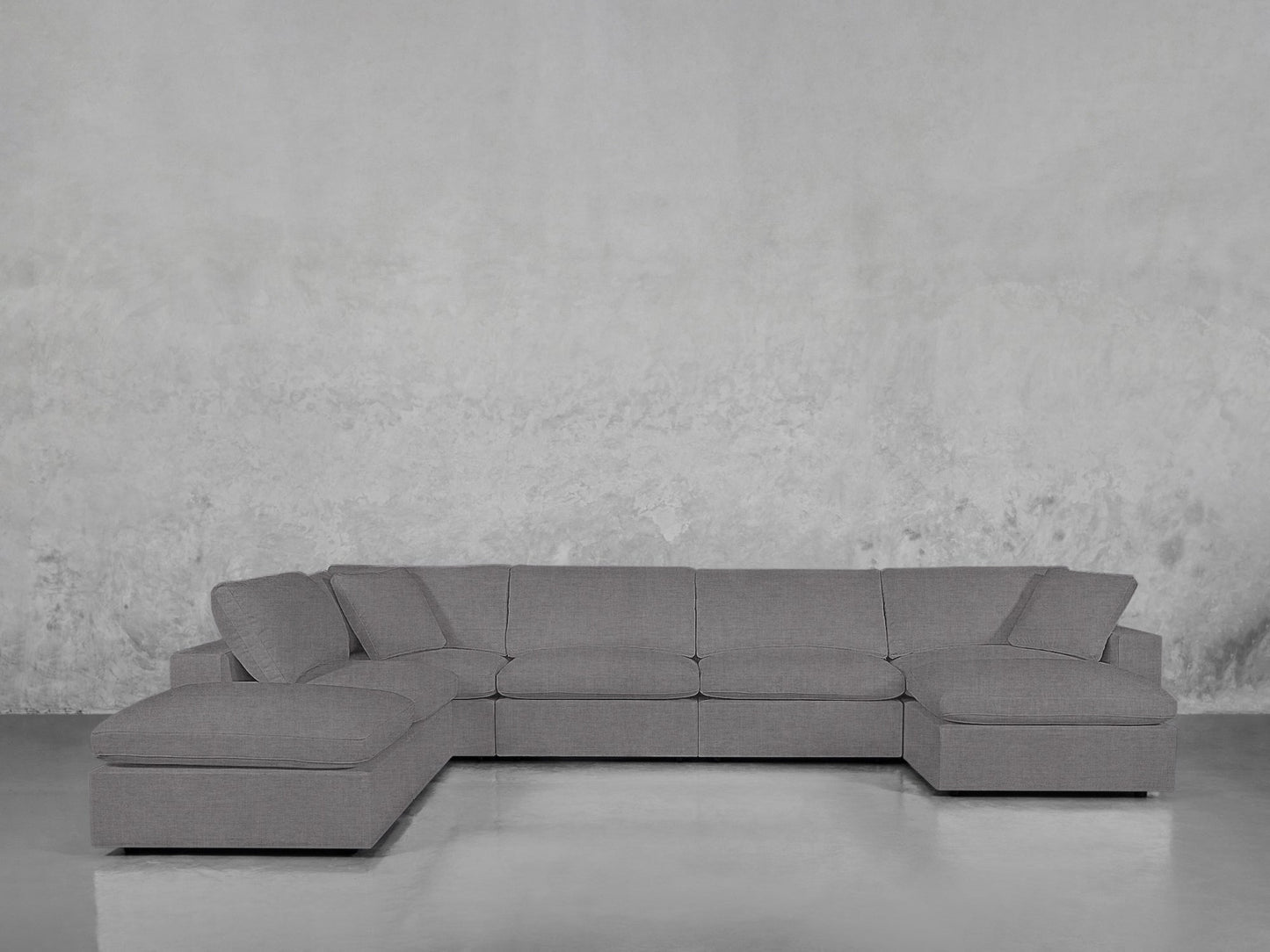 A 7-Seat Modular Chaise Corner Lounger Sectional with clean lines in gray sits on a shiny floor against a textured light gray wall, creating a minimalist, modern look.