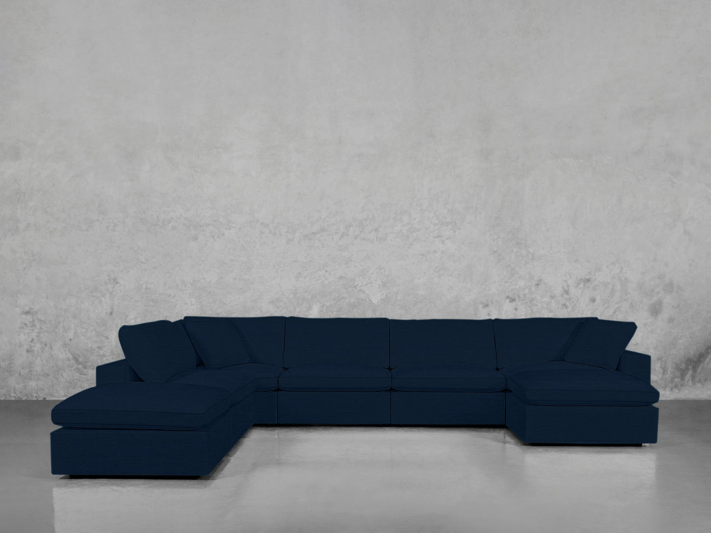 The 7-Seat Modular Chaise Corner Lounger Sectional in dark blue stands against a light gray textured wall, its chaise lounges on both ends reflecting subtly off the sleek floor.