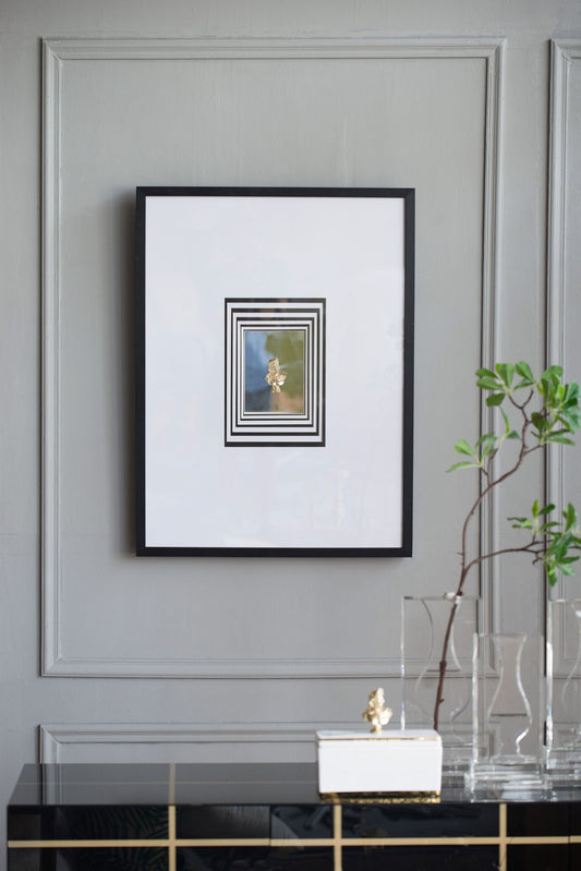 The Modern Minimalist Wall Art With Roman Inspired Bust, featuring a multicolor design, is displayed on a gray paneled wall above a black console with a potted plant and glass decor. Perfect for living rooms, entryways, or bedrooms.