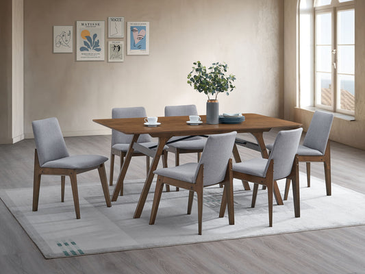 A modern dining room featuring the Kaela Dining Table in walnut, set for six with light gray upholstered chairs, a plant centerpiece, cups, and plates on a light rug. Minimalist wall art and large windows fill the space with natural light.