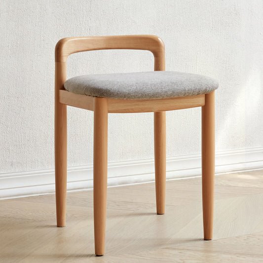 The Stool Bed For Dining Room - Natural, featuring a modern wooden design with a curved backrest and light gray cushioned seat, sits on a light wood floor against a plain white wall.