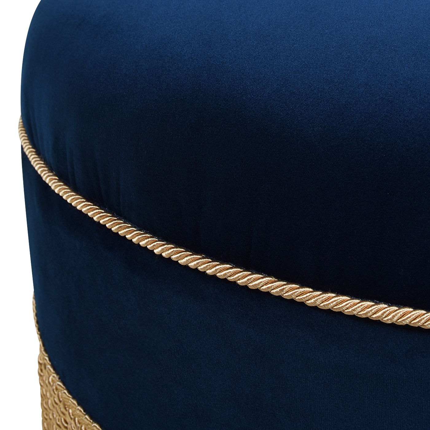 Close-up of the Yolanda Round Upholstered Accent Ottoman in dark blue velvet, featuring gold braided trim wrapped horizontally around its middle and bottom.