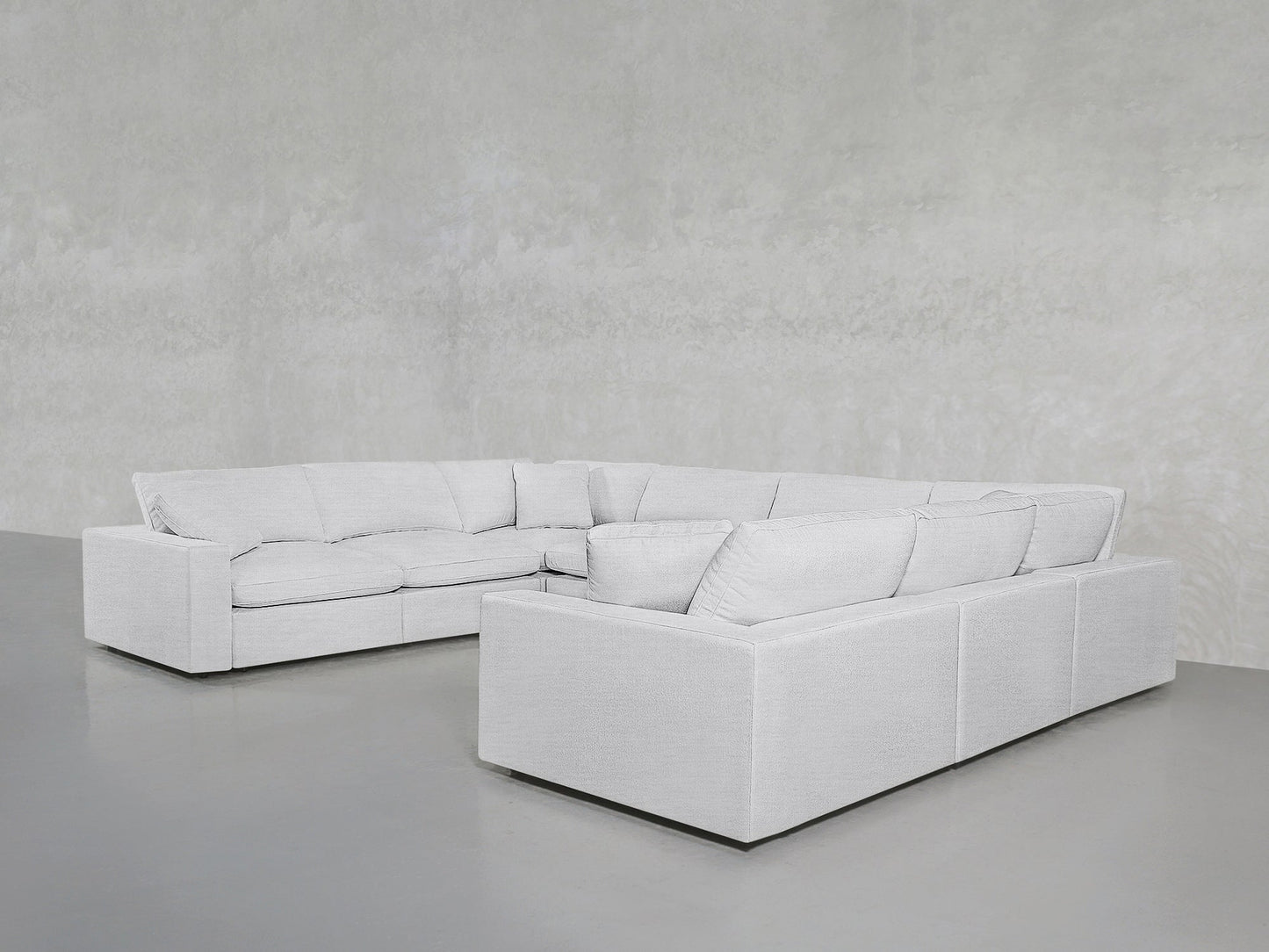 An 8-Seat Modular U-Sectional with thick cushions in light gray is placed in a minimalist room with gray floors and textured gray walls.