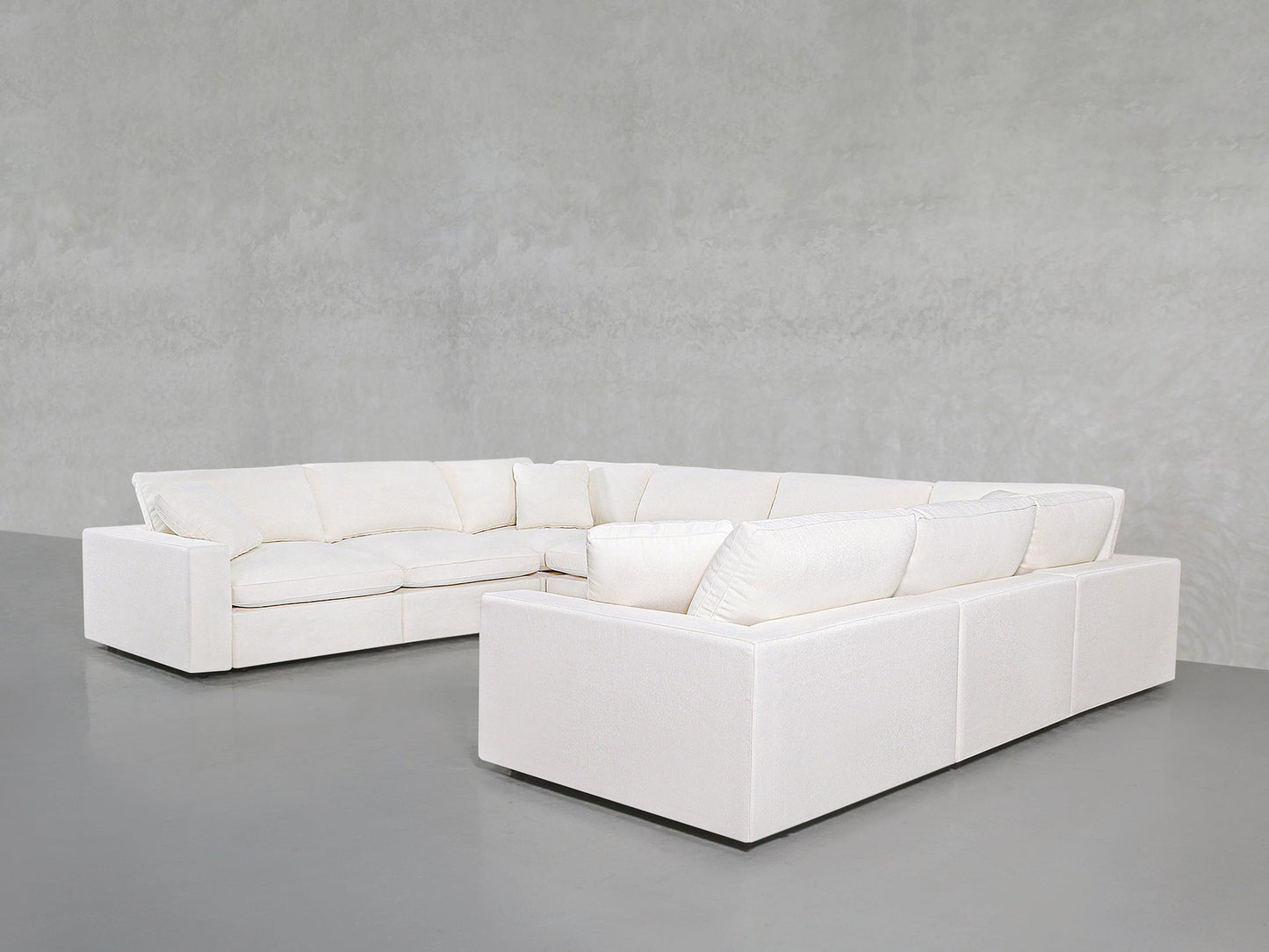 An 8-Seat Modular U-Sectional with plush cushions in white is set in a minimalist room featuring smooth gray floors and a textured light gray wall.
