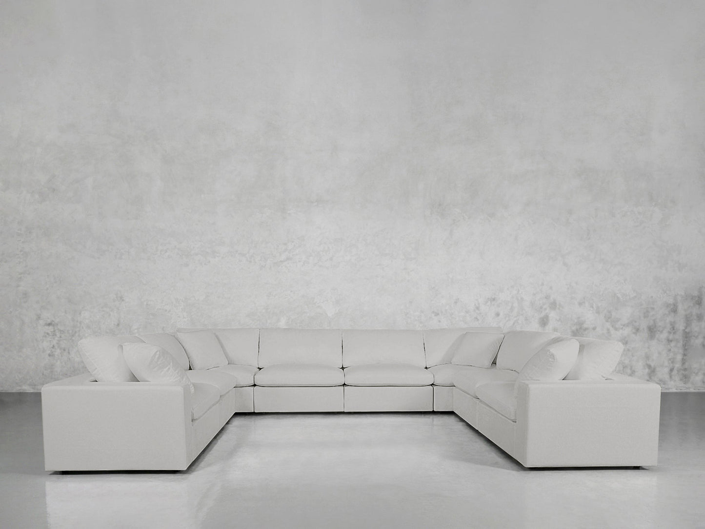 An 8-Seat Modular U-Sectional in light gray with clean lines and low arms sits against a plain, textured light gray wall on a shiny, light-colored floor.