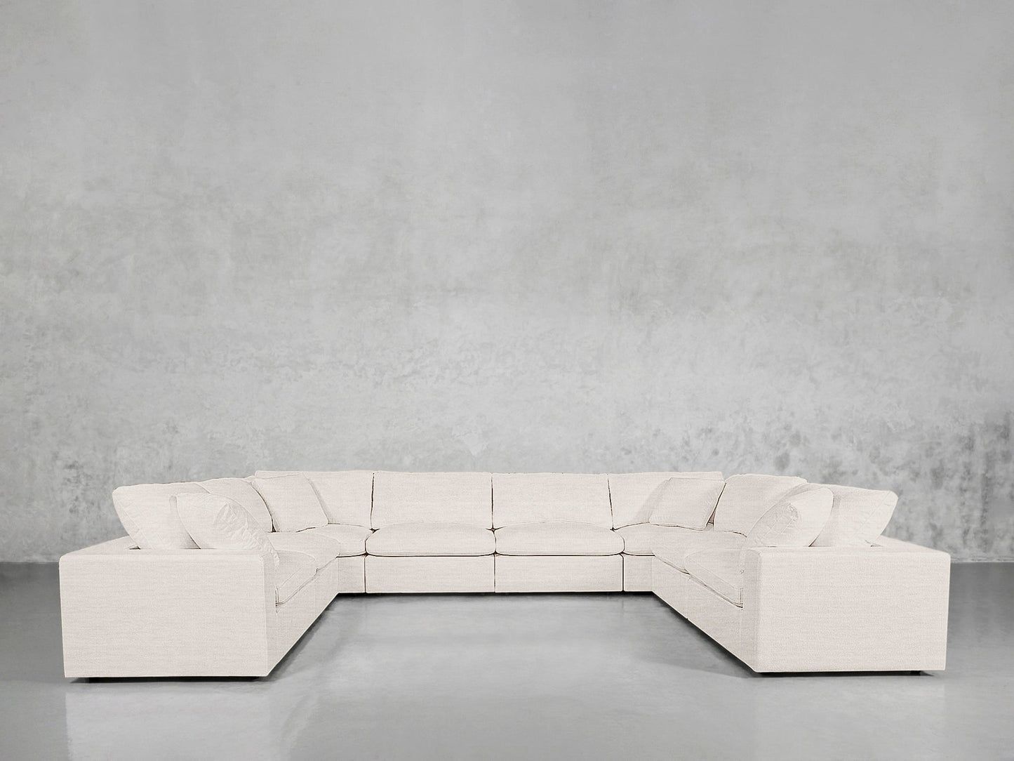 An 8-Seat Modular U-Sectional with a modern white design and plush cushions is placed against a light gray wall in a minimal room featuring a shiny gray floor.
