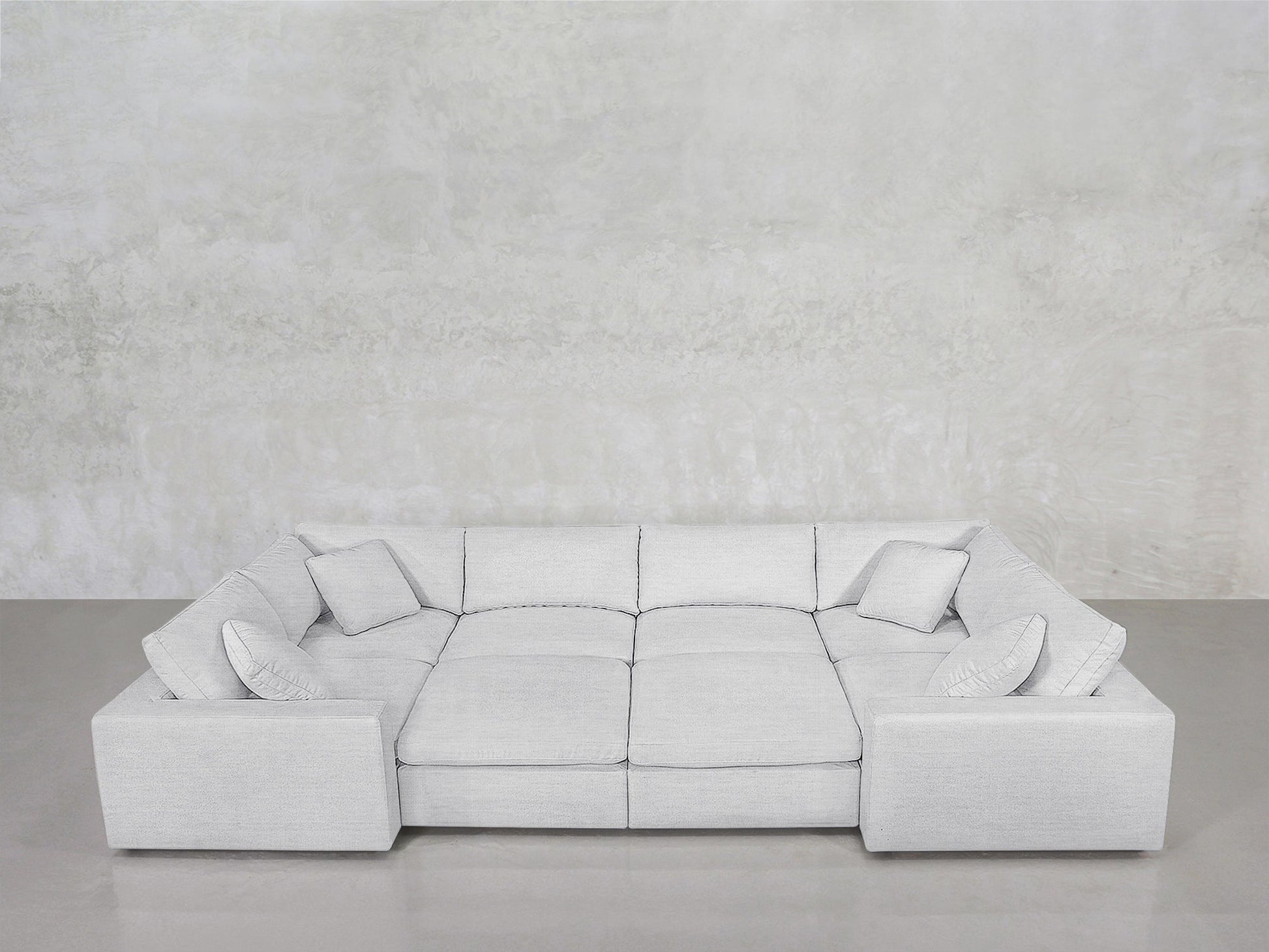The 8-Seat Modular Closed Pit, a modern light gray sectional with four matching cushions, wide armrests, and a low backrest, is set against a textured light gray wall above a smooth gray floor.