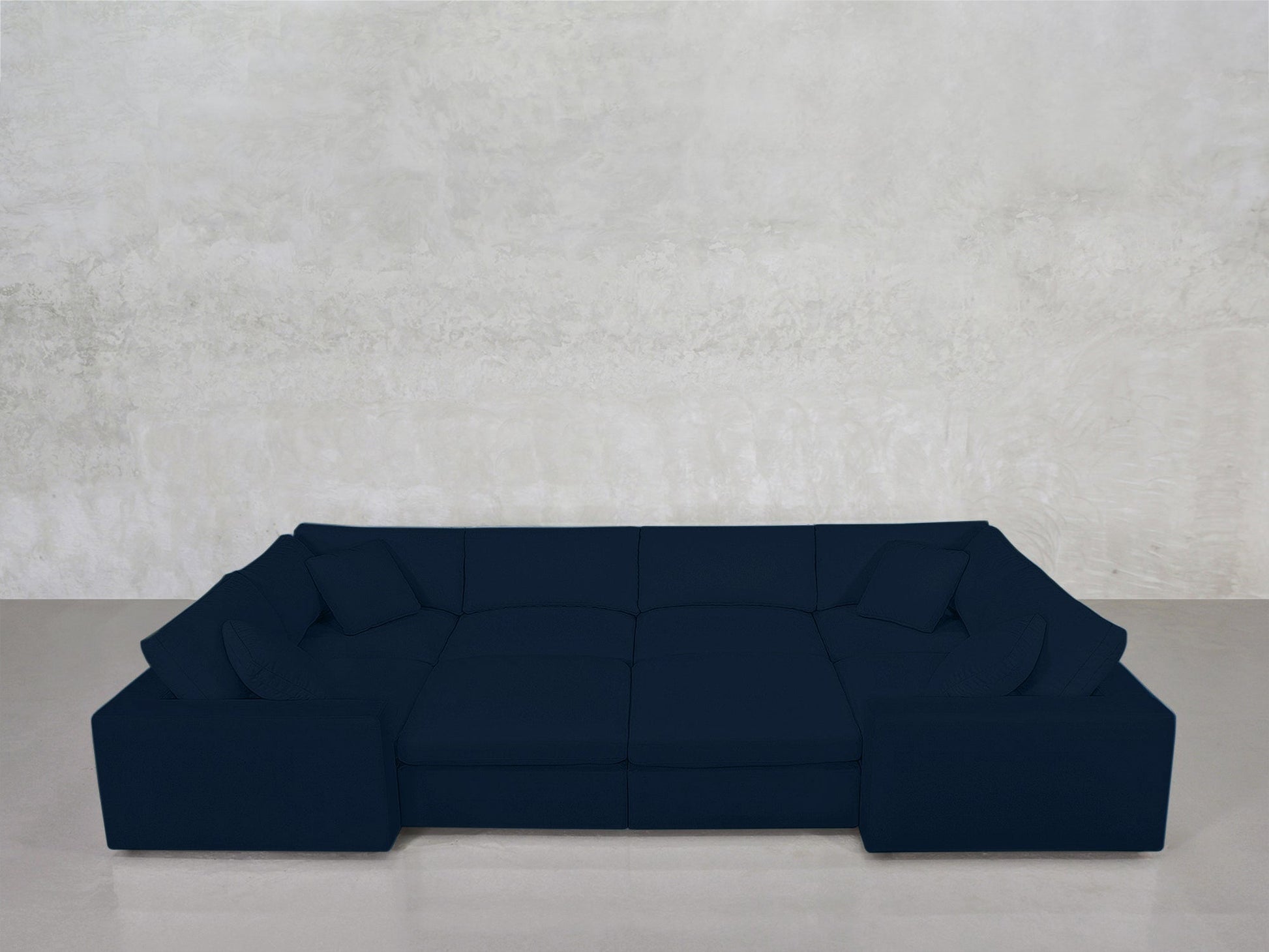 An 8-Seat Modular Closed Pit in dark blue with cushions sits against a light gray textured wall on a smooth, light gray floor.